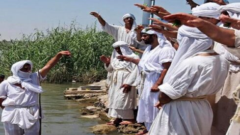 أشخاص بملابس بيضاء يقفون على ضفة نهر في طقوس دينية.