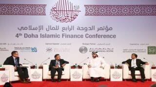 أربعة رجال على منصة بمؤتمر الدوحة الرابع للمال الإسلامي، مع شعارات شركاء المؤتمر في الخلفية.