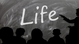 كلمة "Life" مكتوبة باللون الأبيض على سبورة سوداء مع ظلال أشخاص يستمعون لشرح.