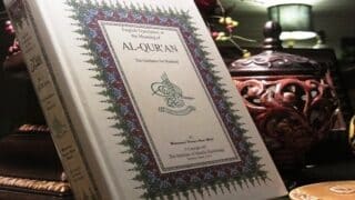 كتاب بالعربية والإنجليزية بعنوان "AL-QUR'AN" على طاولة مزينة بديكور منزلي.