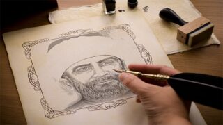 امرأة ترسم بالقلم والحبر على ورق مزخرف لشخص يرتدي عمامة، مع أدوات رسم على المكتب.