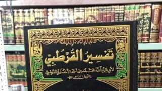 عنوان "تفسير القرطبي" بغطاء مزخرف محاط بكتب على رف مكتبة.