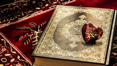 Decorative Quran with gold patterns on red carpet, heart-shaped ornament on top.