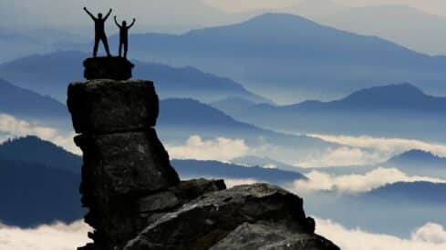 Two people standing on a rocky peak, with foggy hills creating a vast background.