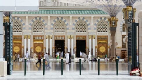 Grand mosque entrance with arches, golden doors, marble pillars, and people in courtyard.