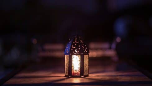 Illuminated lantern with moon and star cut-outs on a surface, casting a warm glow in darkness.