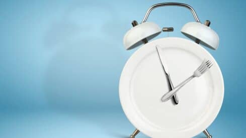 Clock design using a plate with fork and knife hands, silver bells on top, light blue backdrop.