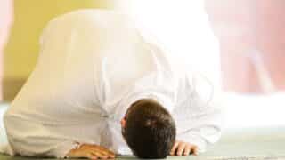 Person kneeling with forehead and hands on ground in white attire, bright setting.