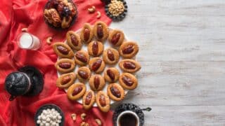 Table with pastries topped with dates, nuts, sweets, milk, and coffee on red fabric.