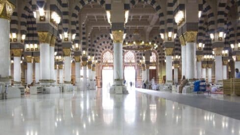 Interior of a grand mosque with marble columns, gold accents, chandeliers, and people inside.