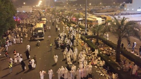 Large crowd in white on busy city street at night, with buses and palm trees lining the area.