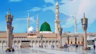 Large prophet mosque with green dome, minarets, ornate details, courtyard, and clear blue sky.