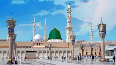 prophet mosque complex with green dome, minarets, courtyard, lamp posts, blue sky.