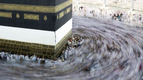 People in white garments circle the Kaaba, a black-draped structure with calligraphy, in a mosque.