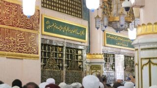 prophet grave interior with Arabic calligraphy, metal grille, and crowd at a religious site.