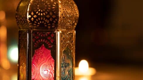 An Arab lantern with colored decorated glass that emits light in a dark background.