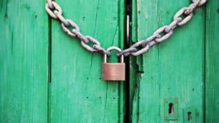 Padlock secures a chain on a weathered green wooden door.