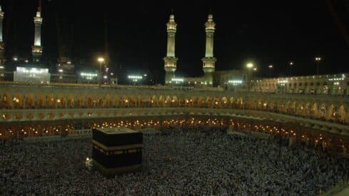 A night view of the honorable Kaaba in the Grand Mosque in Mecca, surrounded by worshipers and illuminated minarets.