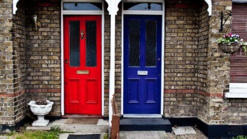 Two adjacent doors, red on the left and blue on the right, surrounded by brick walls and floral decorations.