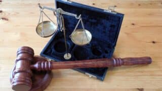 Wooden gavel and block beside a brass scale in an open velvet-lined case on a wooden surface.