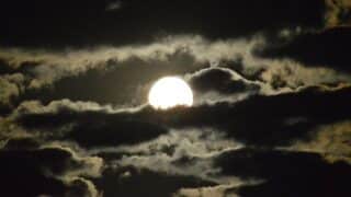 Full moon partially hidden by dark clouds in a dramatic night sky scene.