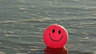 Pink smiling ball floating on water with gentle ripples around.