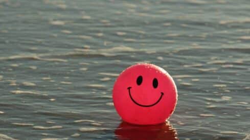 Pink smiling ball floating on water with gentle ripples around.