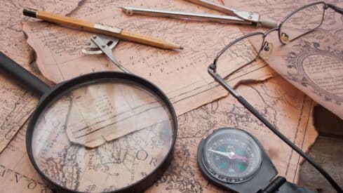 Vintage navigation tools with magnifying glass, compass, eyeglasses, pencil, and map.