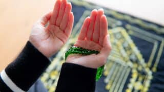 Person's open hands with green beads; gold-patterned carpet in background.