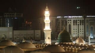 Al-Masjid an-Nabawi at night with illuminated minaret and green dome, Medina, Saudi Arabia.