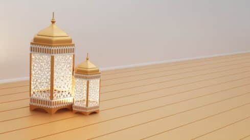 Two patterned lanterns emit a warm glow on a wooden floor, with a plain background.