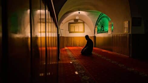 Person kneeling on carpet in dim room with wooden paneling, arched ceiling, serene atmosphere.