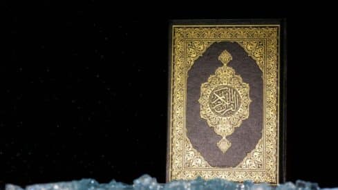 Ornate holy Quran cover with gold patterns on dark background, crystalline foreground.