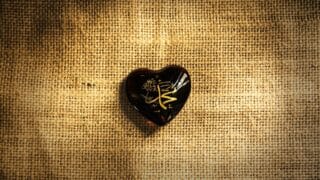 Heart-shaped dark ornament with golden Arabic calligraphy Mohamed word on burlap surface.