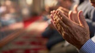 Hands in prayer position on red carpet, background softly blurred with similar postures.