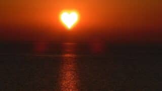 Sunrise or heart-shaped sunset on the sea, with orange light reflection.