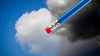 Blue pencil with red eraser against clouds under blue sky transitioning to dark.