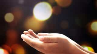 Hands held together, palms up, with colorful, blurred lights in the background.