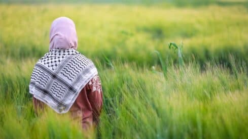 Person in pink headscarf and shawl in lush green field with tall grass.