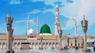 prophet Mosque with green dome, minarets, people on marble courtyard, lamp posts, blue sky.