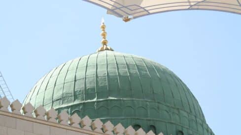 prophet mosque with Green dome with gold finial against blue sky, framed by architectural elements.