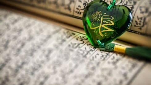 Green heart-shaped pendant with gold Arabic calligraphy on holy Quran.