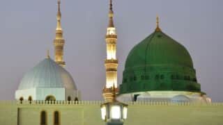 View of Prophet's Mosque, Medina, featuring illuminated green and white domes with minaret.