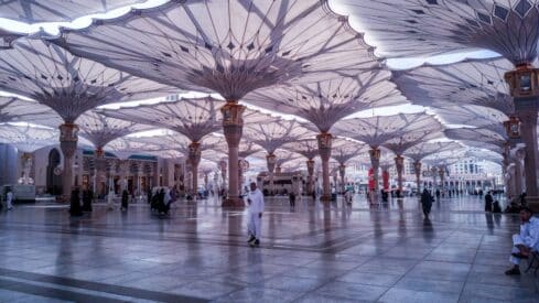 Architectural scene with large canopies in a public space, people walking on tiled ground.