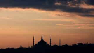 Silhouette of a mosque with minarets against a dramatic sunset and cloudy sky.