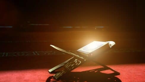 Open book on a wooden stand, warmly lit on a red carpeted surface.