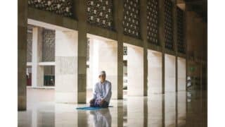 Person in white sits on blue mat in spacious, tiled hall with columns and patterned walls.