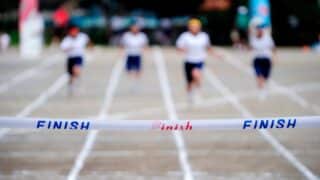 Runners approach a finish line with "FINISH" in blue and red on white tape, unbroken.