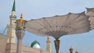 Courtyard view with folding umbrellas, minarets, and mosque's green dome under a clear sky.