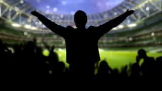 Silhouette of a person with arms outstretched in a stadium, facing a crowd.